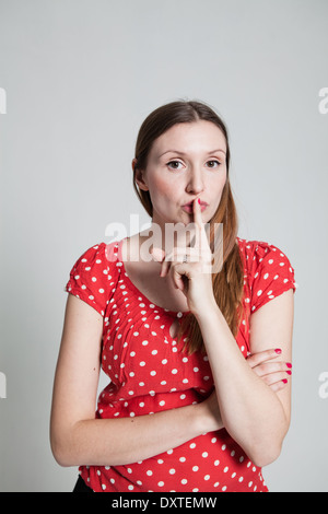 Studio portrait of attractive woman with finger over pursed lips to signal for quiet Stock Photo