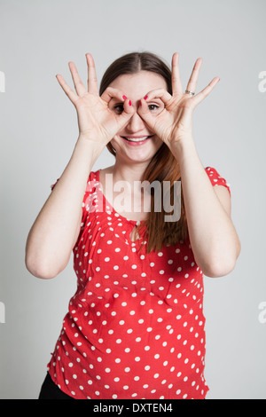 Studio portrait of smiling attractive woman looking through finger goggles Stock Photo