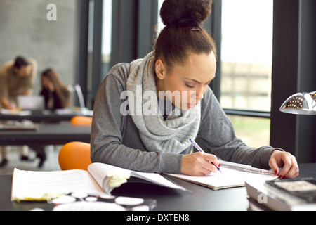 Female student taking notes from books for her study. Young african american woman sitting at table with books for information.