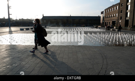 Women walking past fountain outside UAL Central St Martins Art College in Granary Square, Kings Cross London N1  KATHY DEWITT Stock Photo