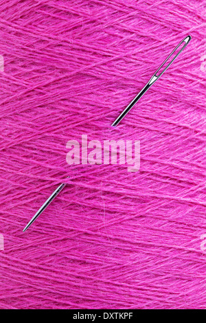 close up of long stainless needle stuck in purple wool texture thread Stock Photo