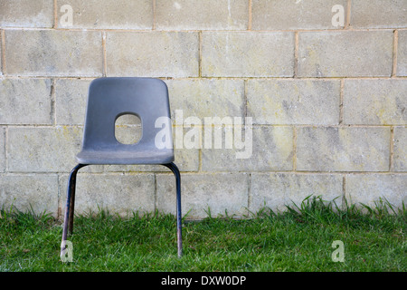 Abandoned empty plastic chair on grass in front of a concrete block wall