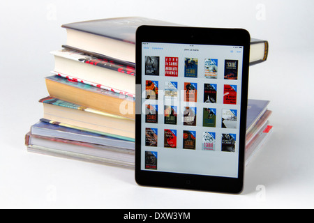Apple iPad mini displaying icons for 21 books with a stack of only 6 printed paper books Stock Photo