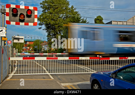 Blue car waiting at a railway level crossing as a blue commuter train speeds past.. Stock Photo