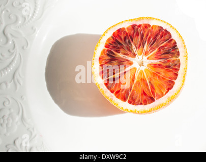 Red orange sliced with shadow on white plate with patterned edge. Stock Photo