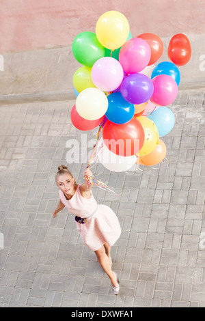 top view of pretty young girl in pink dress holding a bunch of balloons Stock Photo