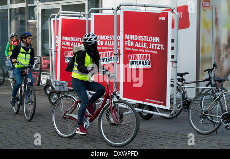 Berlin, Germany. 01st Apr, 2014. Tourists cycle past mobile advertisement banners of the new minimum wage campaign of the DGB with the slogan 'Minimun wage for all, now. Dignity knows no exceptions: No wages under 8.50 euros' in Berlin, Germany, 01 April 2014. Photo: BERND VON JUTRCZENKA/DPA/Alamy Live News