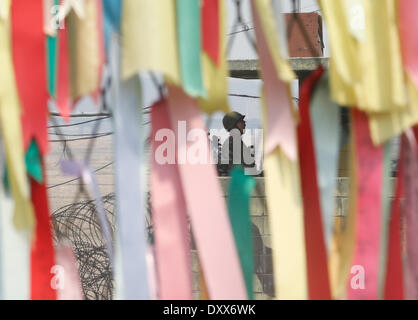 Paju, South Korea. 1st April 2014. A South Korean soldier on a guard post is seen through a military fence decorated with ribbons on which people have written their hopes for the peace between the two Koreas, near DMZ, Paju, South Korea, on Tuesday April 1, 2014. North and South Koreas exchanged artillery fire across the western maritime border, the Northern Limit Line (NLL) in the West (Yellow) Sea on Monday after the North conducted a live-fire drill that sent artillery shells into waters of the South, while the U.S. and South Korea were holding their largest joint landing operation drills i Stock Photo