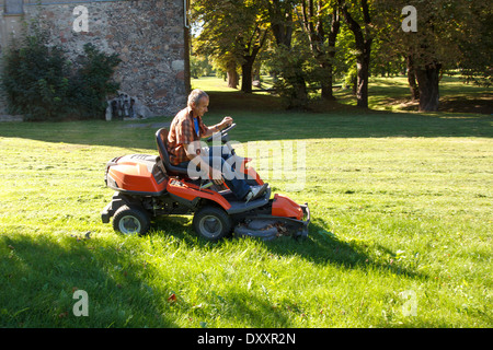 man driving a red lawn mower (tractor) in the city park Stock Photo