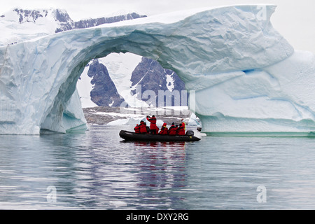 Antarctica tourism with cruise ship passengers in zodiac boat viewing Antarctic glacier and iceberg, ice berg with arch. Stock Photo