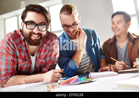 Friendly guys choosing colors from palette, bearded man in eyeglasses looking at camera Stock Photo