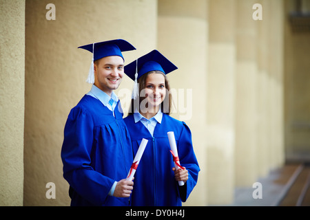 Two happy students in graduation gowns looking at camera Stock Photo