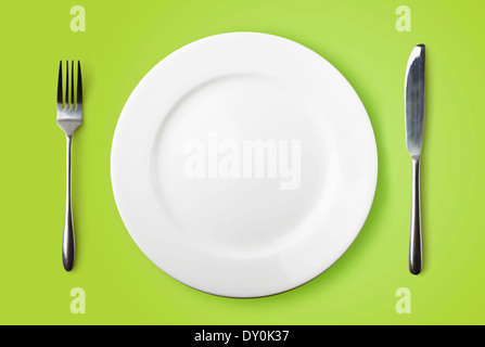 Empty plate, fork and knife on green background Stock Photo