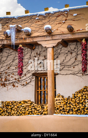 Stacks of firewood under portico of a Pueblo Revival style building in Santa Fe, NM charms with hanging ristas & icicles & snow Stock Photo