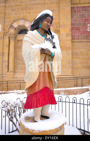 Bronze statue of Saint Kateri wearing turquoise in snowy scene standing in front of the Cathedral Basilica of St. Francis of Assisi, Santa Fe, NM, Stock Photo
