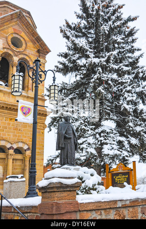 A bronze statue of Jean Baptiste Lamy stands before Basilica Cathedral of St. Francis of Assisi on a snowy day in Santa Fe, NM Stock Photo