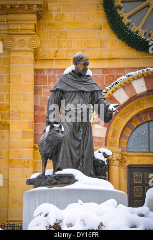 A snow covered bronze statue of St. Francis stands in front of the Cathedral Basilica of St. Francis of Assisi, Santa Fe NM Stock Photo