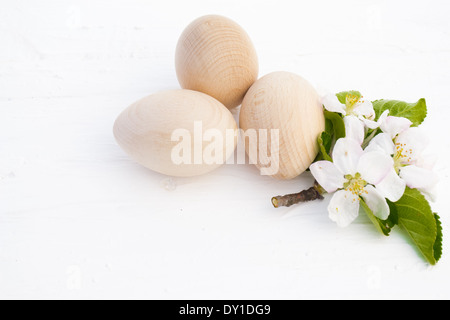 Three wood/wooden eggs and an apple blossom in the centre on display in natural light. Stock Photo