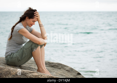 Upset and depressed woman sitting by the ocean crying with her head in her hand.
