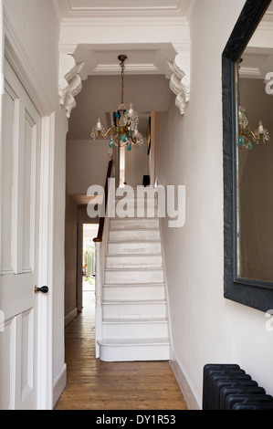 White wooden staircase in hallway with corbels and blue drop chandelier. Stock Photo