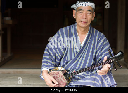 Elderly Okinawan man with sanshin in traditional yukata at Ryukyu Mura, Yomitan Village, Okinawa, Japan Stock Photo