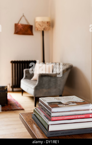 Pile of books on wooden coffee table with buttoned sofa and old radiator in background Stock Photo