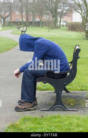 Male wearing hoodie sitting on park bench Stock Photo