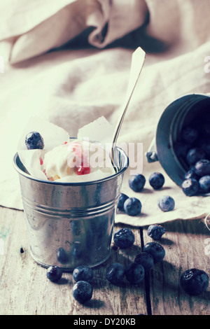 Ice cream, served in little metal pail with blueberries on white wooden table in retro filter effect. Stock Photo