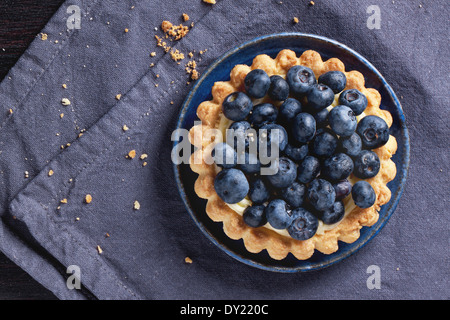 Top view on blueberry tart served on blue ceramic plate over textile napkin. Stock Photo