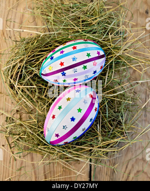 Two easter eggs, decorated with multicolored braid and sparkles in the hay on the background of wooden boards on top Stock Photo