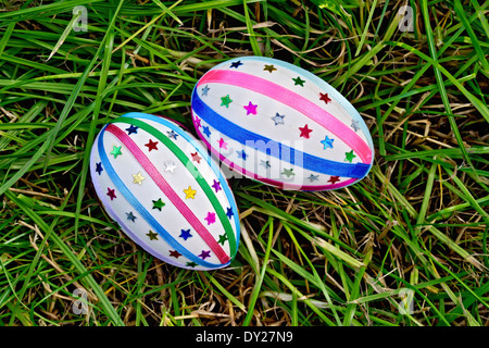 Two easter eggs, decorated with multicolored braid and sparkles as asterisks on green grass top Stock Photo