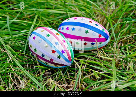 Two easter eggs, decorated with multicolored braid and sparkles as asterisks on the green grass Stock Photo