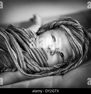 Black and white photo of cute little baby girl wrapped in scarf, lying down on the bed, kids fashion concept Stock Photo