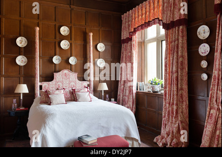 Toile de jouy curtains and bed dressings by Design Archive in bedroom with wooden wall panelling and decorative china plates Stock Photo