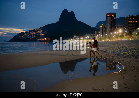 Couple walking along Ipanema beach at night,with twin peaks of Two Brothers mountain at Leblon, in background, Rio de Janeiro, B Stock Photo