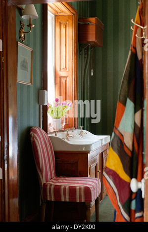 A horseshoe chair covered in Pennant striped linen by Oka in bathroom with dark green Soho striped wallpaper from Cole and Son Stock Photo