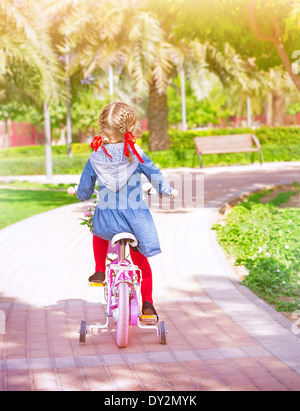 Little girl riding on the bicycle, back side, active childhood, cute little cyclist, summer vacation, healthy lifestyle Stock Photo