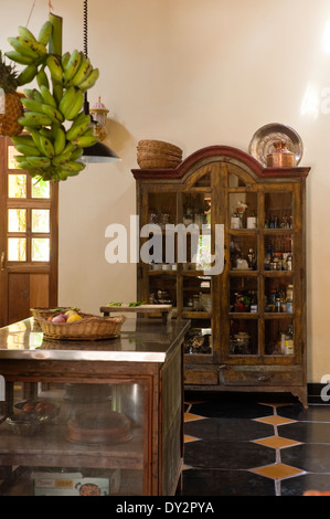 Glass-fronted cabinet and freestanding unit with bananas hanging in Goan kitchen Stock Photo