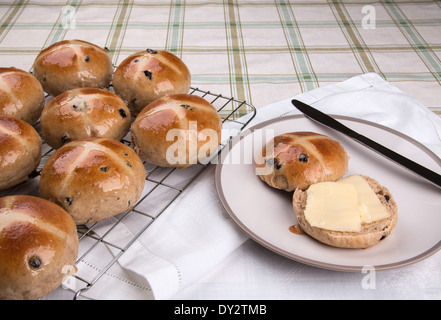 Hot cross easter/buns on a wire cooling rack with one bun sliced open with butter on (15 of a series of 24) Stock Photo