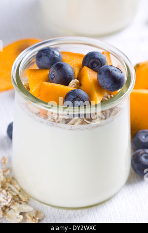 Close up of yogurt in glass jar topped with cut persimmon and blueberries Stock Photo