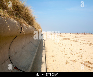 Wave return wall coastal defence and wide sandy beach submerging wooden groyne, Horsey, Norfolk, England Stock Photo