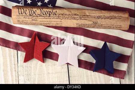 A rolled up US Constitution on an American Flag with red white and blue stars in the foreground. High angle shot on rustic table Stock Photo