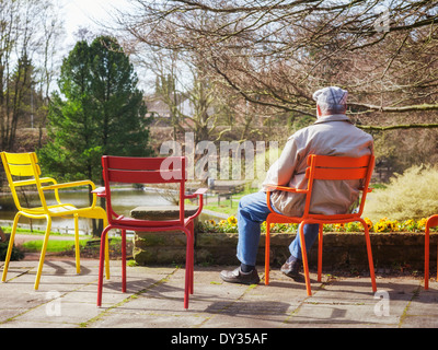 Rear view of elderly man sitting on chair in early spring park Stock Photo