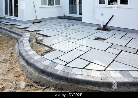 Paving slabs being laid as a patio to back garden of detached house after completion of rear extension Essex England UK Stock Photo