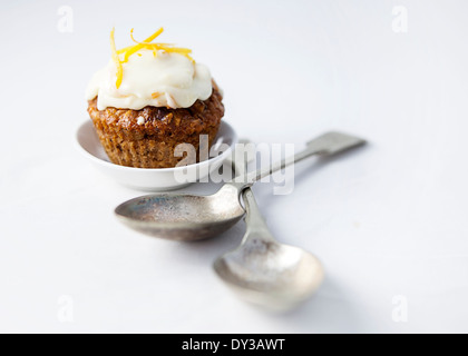 Carrot cake cupcake with citrus cream cheese frosting and vintage spoons in landscape orientation on a high key backdrop Stock Photo