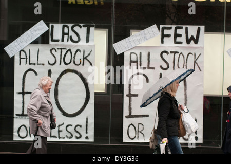 Shop closing down sale signs in a shop front with people walking past. Stock Photo