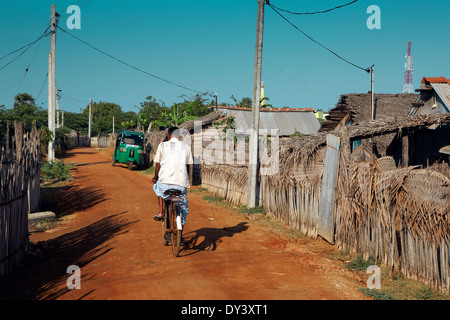 Man riding bicycle in dirt street of poor neighborhood of Mannar, where many refugees from the civil war have been rehoused. Stock Photo