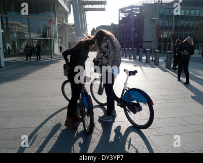 Young women cyclists looking at phone with "Boris bikes" hire bikes at the base of the Shard in London UK KATHY DEWITT Stock Photo
