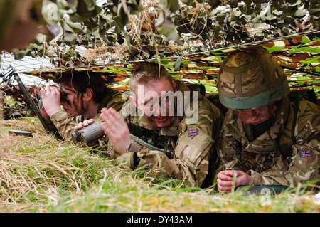 Three soldiers hide underneath camouflage netting in a forward observation post Stock Photo