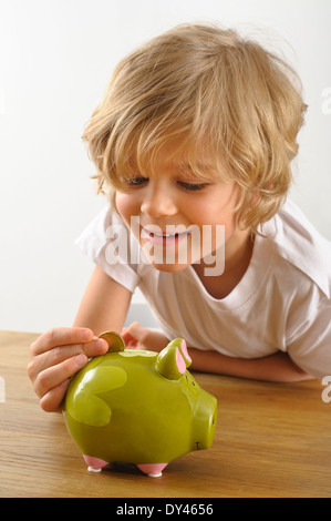 young boy puts a coin into his piggy bank Stock Photo